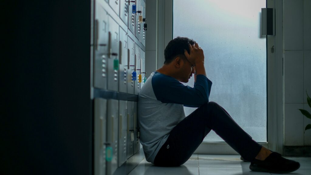 yosi-prihantoro-gXUEQEtpjMs-unsplash A man sitting on the floor of a locker room, looking worried