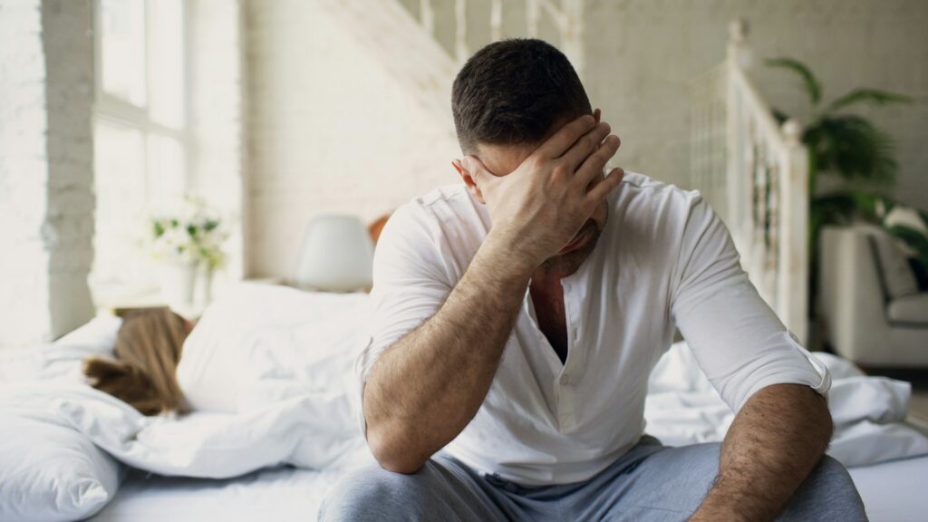 man sitting on bed with hands on face