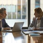 a professional office setting captures a focused discussion between two individuals seated at a sleek conference table, with legal documents and a laptop open between them, highlighting the serious considerations involved in modifying spousal support agreements in texas.