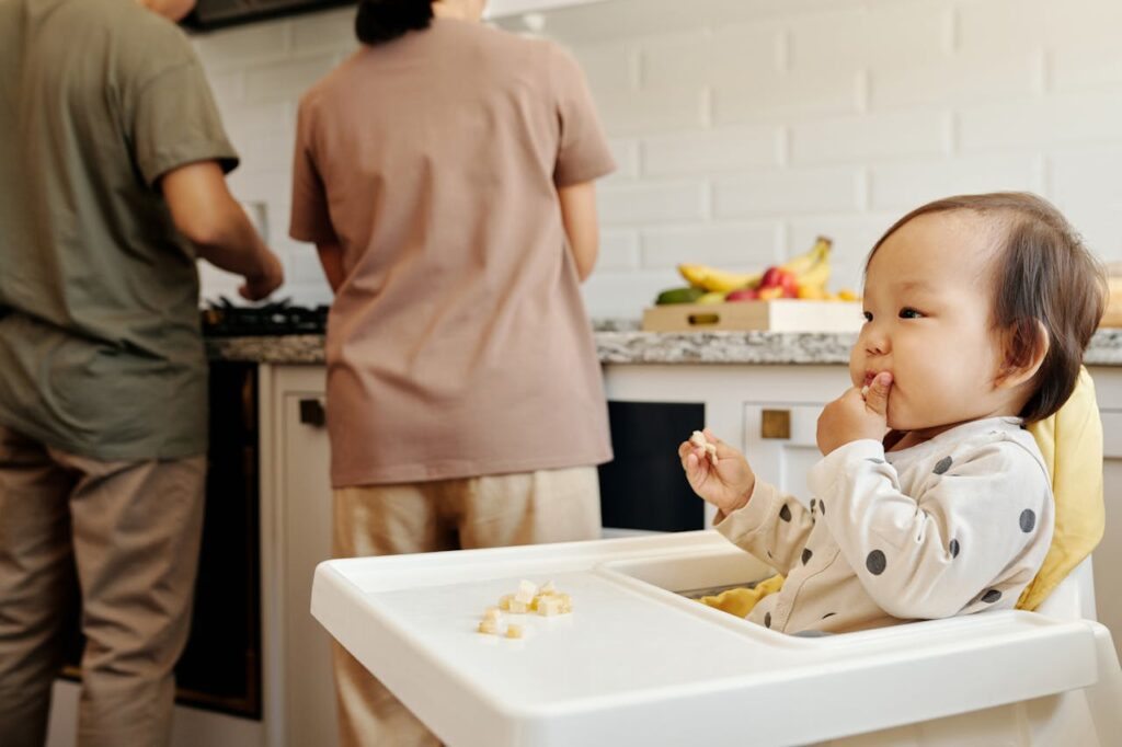 A child sitting on a high chair with 2 adults in the background