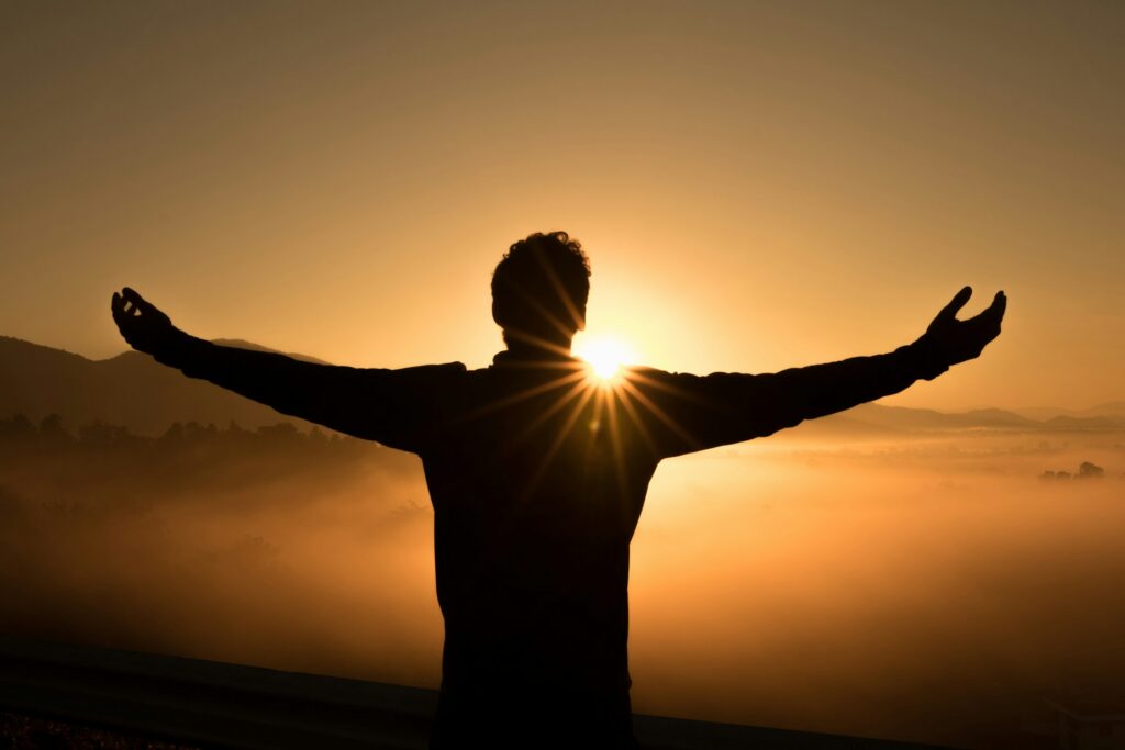 silhouette image of a man with arms raised while looking at sunset
