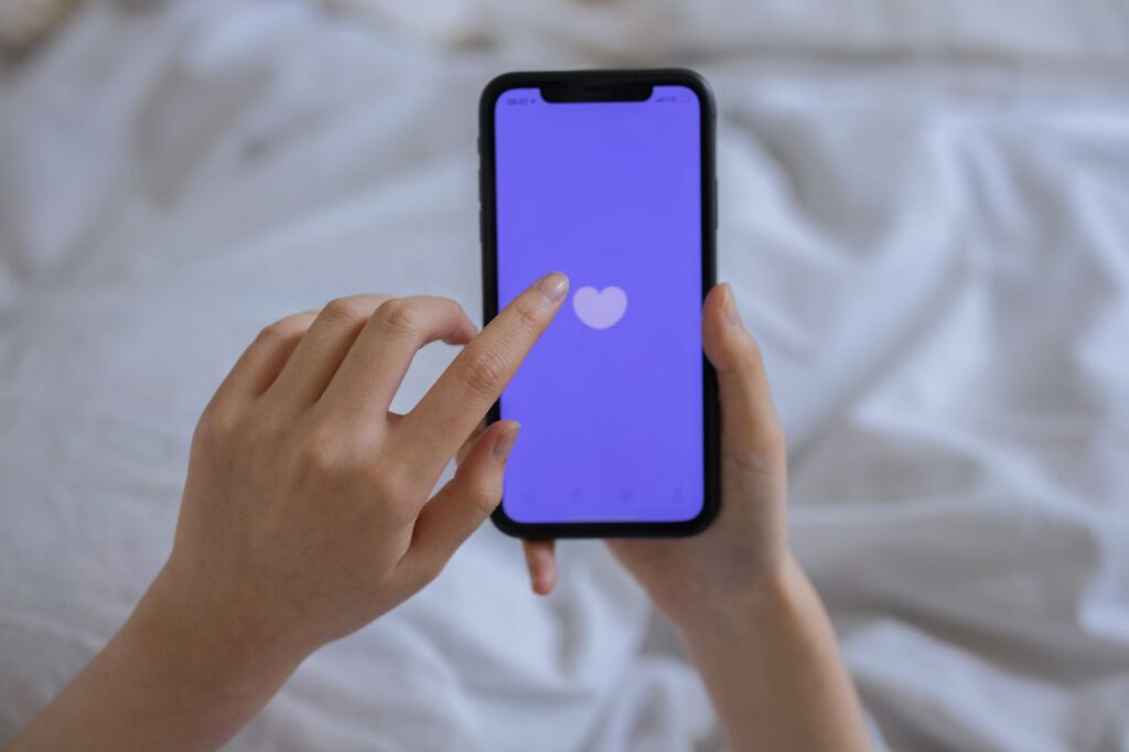 person using a phone in bed, touching a heart icon