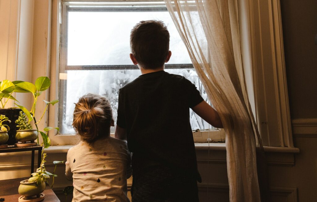 two kids standing near a window