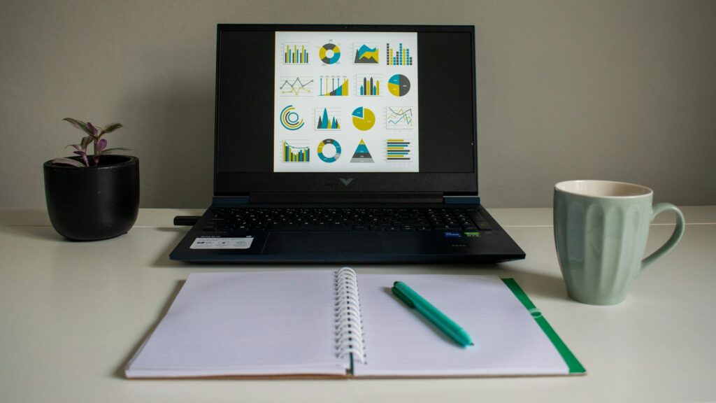 laptop displaying charts beside notebook and mug