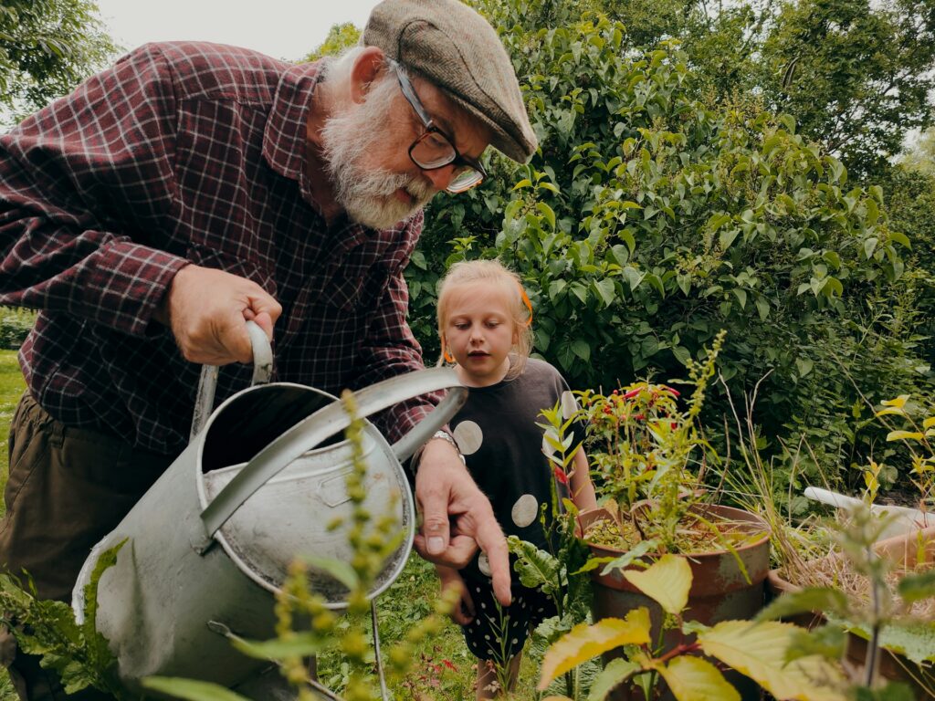 an old man watering plants and a child looking