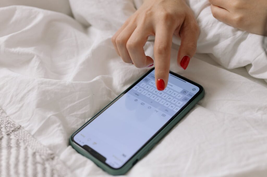 woman wearing red nail polish composing a message on phone