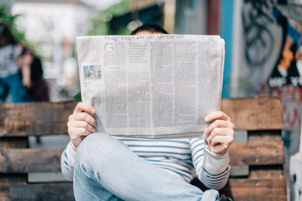 person reading newspaper while sitting on a bench