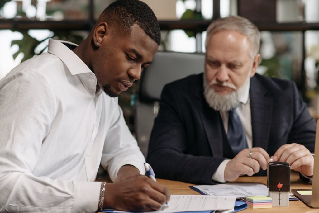 a man in suit looking at another man writing on a document