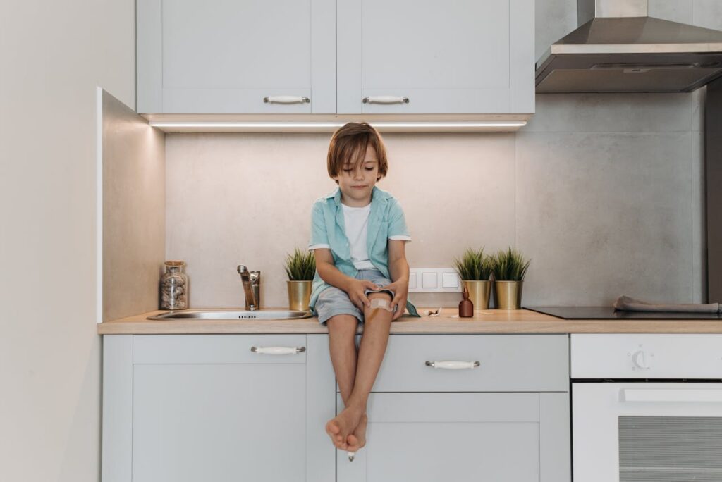 boy with plaster on knee sitting on top of kitchen counter