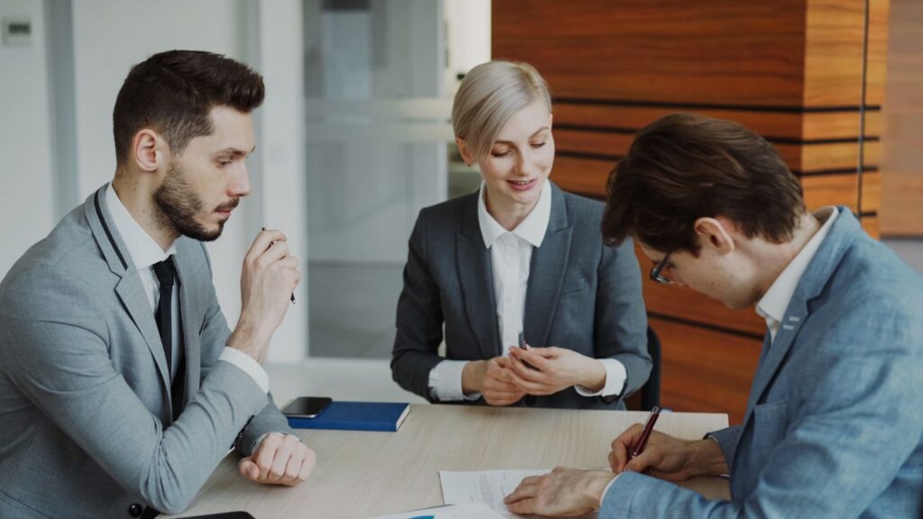a person signing a document while two people witness