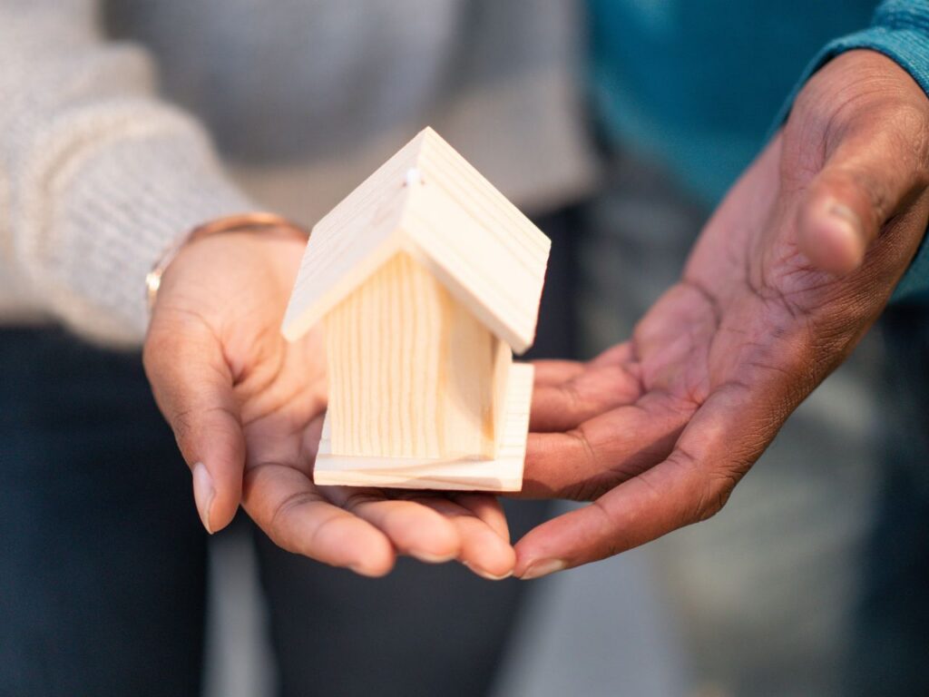 two people holding a miniature wooden house