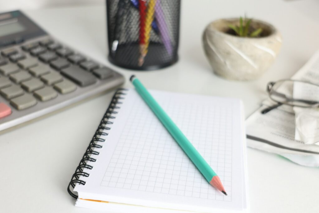 cht-gsml-QfQW294I8sQ-unsplash desk with calculator, notebook, and pencil