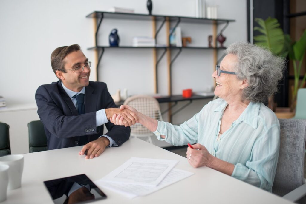elderly person shaking hands with a man dressed in suit