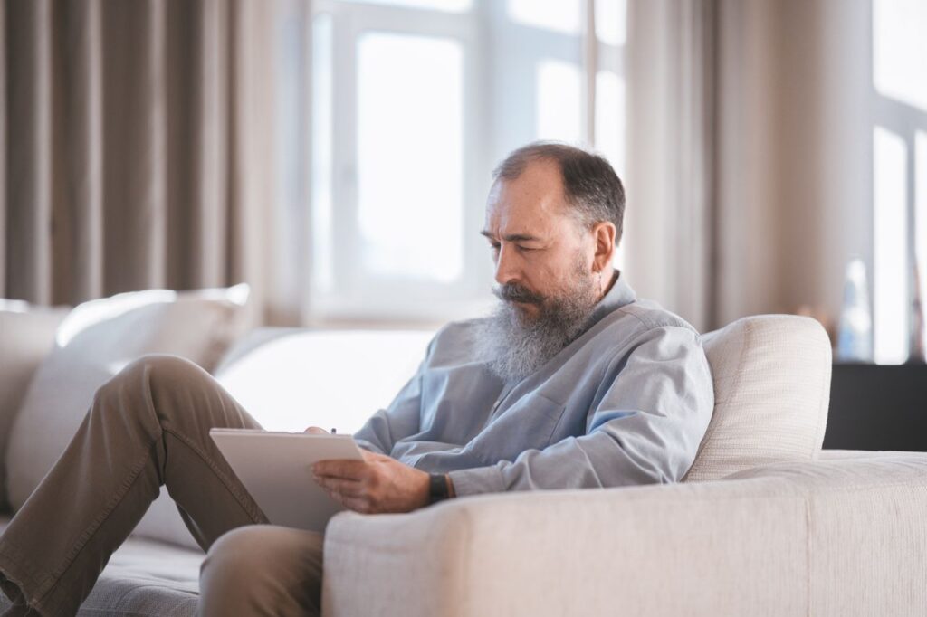 an elderly person sitting on the couch writing