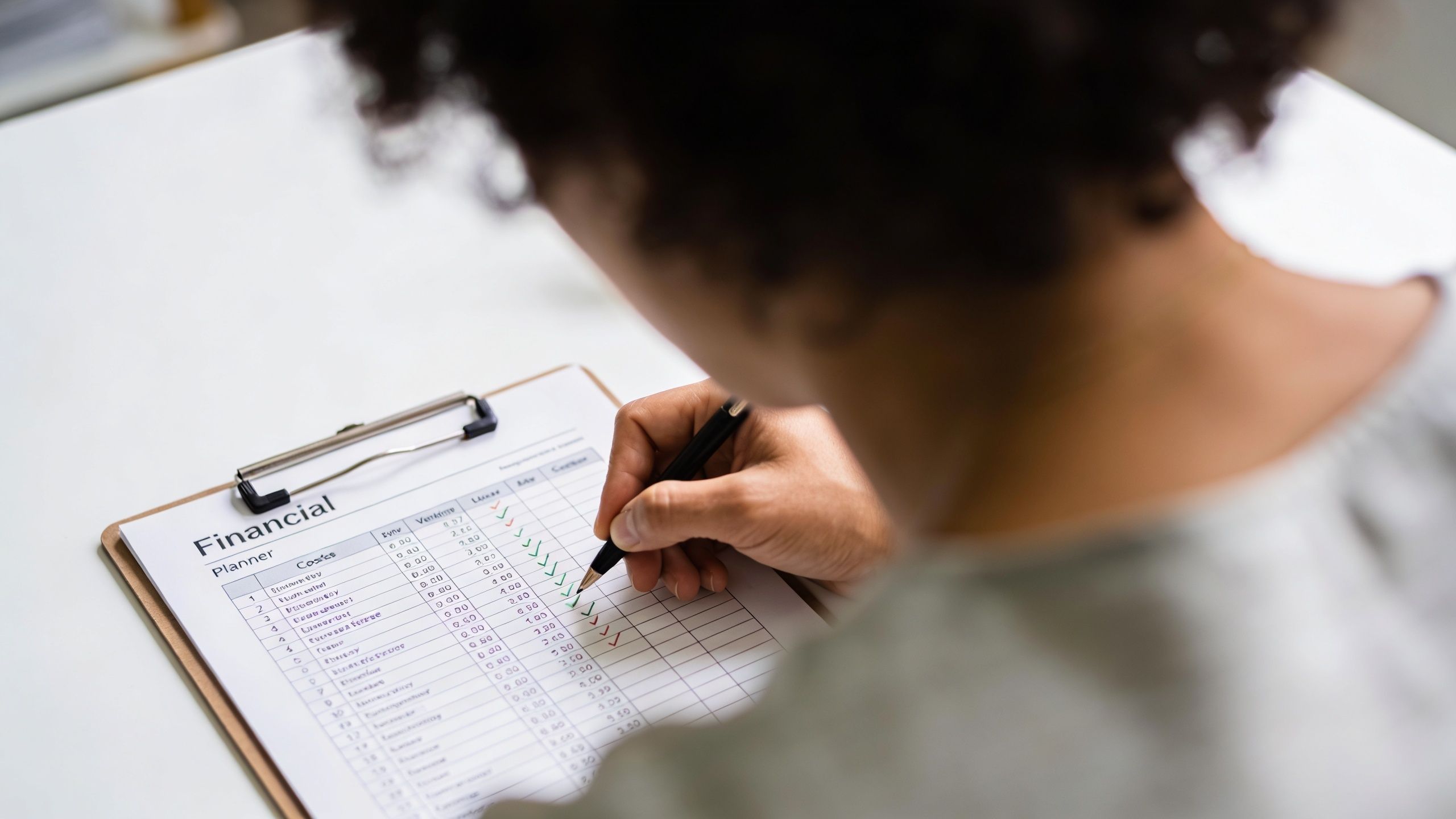 A person writing on a financial planner document on a clipboard while seated at a desk.