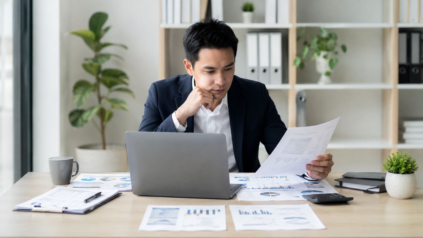 A professional businessman analyzing financial documents and data reports at his modern office desk.