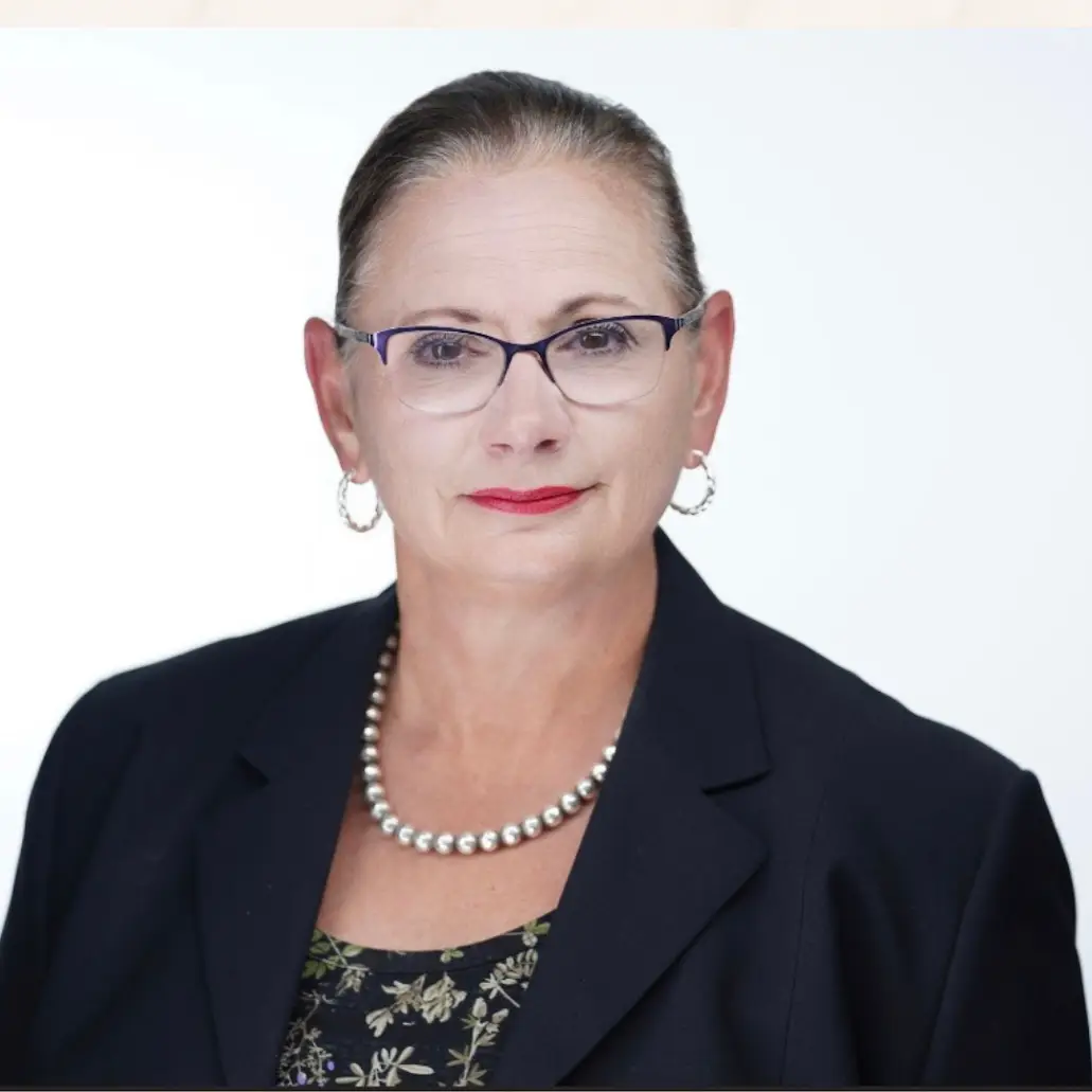 Professional headshot of Anne Gibson wearing glasses and a navy blazer.
